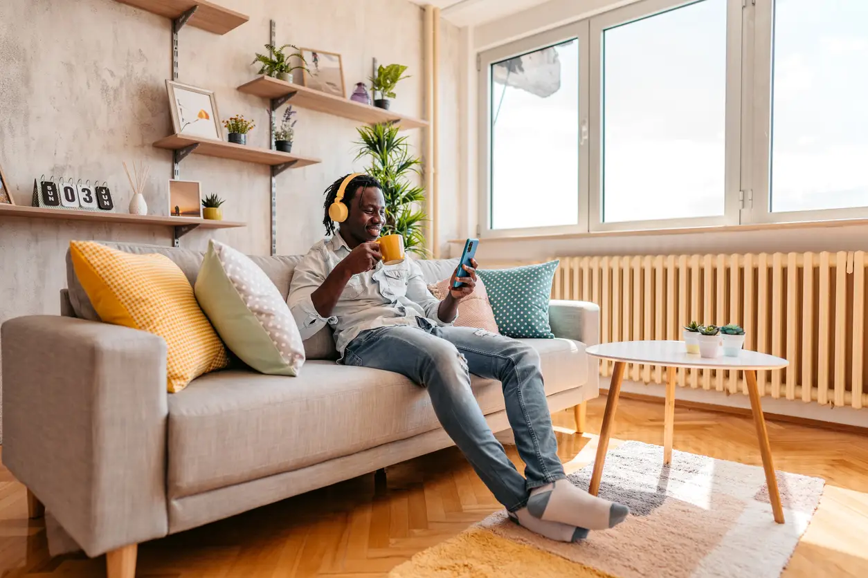 Man in headphones using a smartphone on a couch.